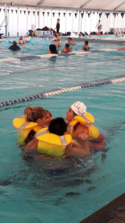Four people in life jackets in a pool pushed up close to each other in a huddle