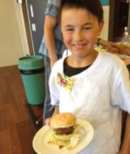 Marc standing, smiling and holding a plate with his burger