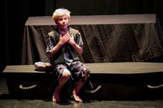 Oliver sitting in costume on a bench on the stage