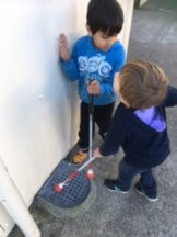 Tane and Robert standing by the drain using the tips of the cane to touch it