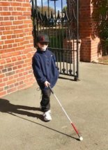 Young boy walking away from the wall holding his cane out in front of him