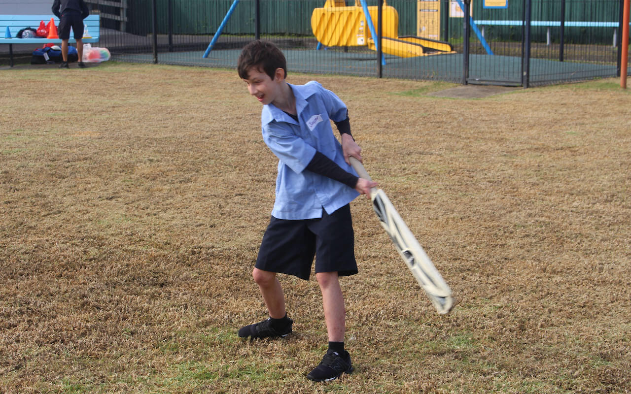 A young boy holding a cricket bat swings at the ball