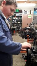 Darcy is attaching a timing-belt to an engine on a stand in the Automotive workshop