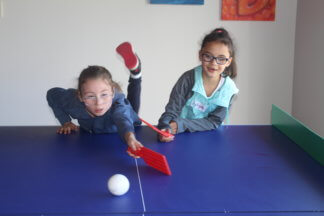 Two girls stretch across the polybats table endeavouring to hit the ball