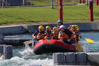 6 young people and 1 guide in a raft going through a rapid at an adventure park