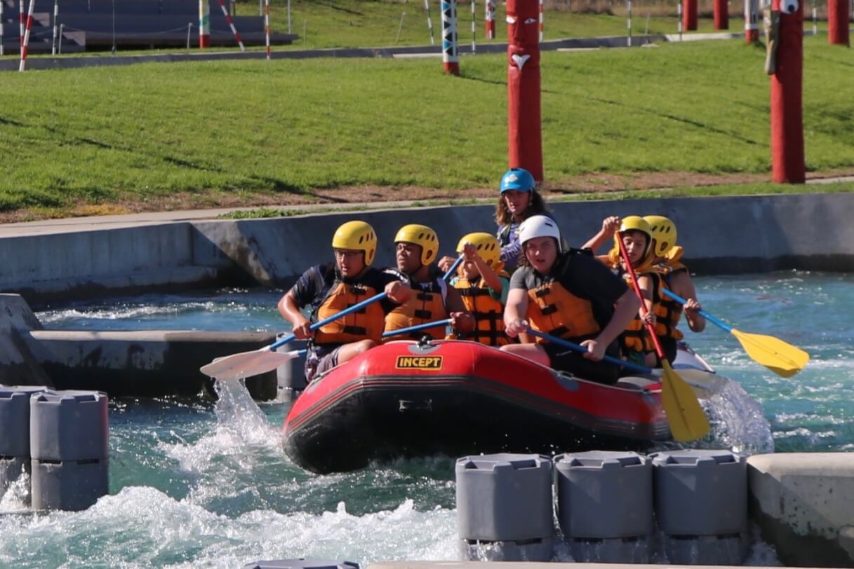 6 young people and 1 guide in a raft going through a rapid at an adventure park