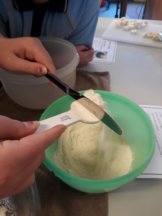 A student is using a knife to level off a quantity of mixture from the bowl on the bench