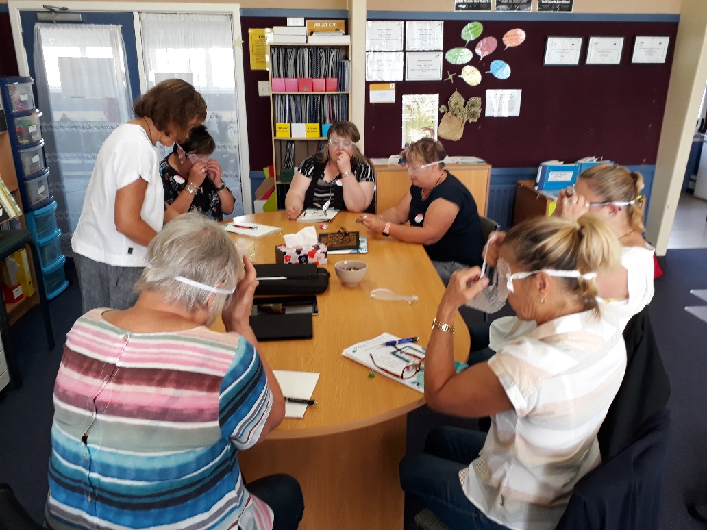 a group of 7 teachers are sitting around a table trying on a variety of sim specs (goggle with bubble wrap over the top)