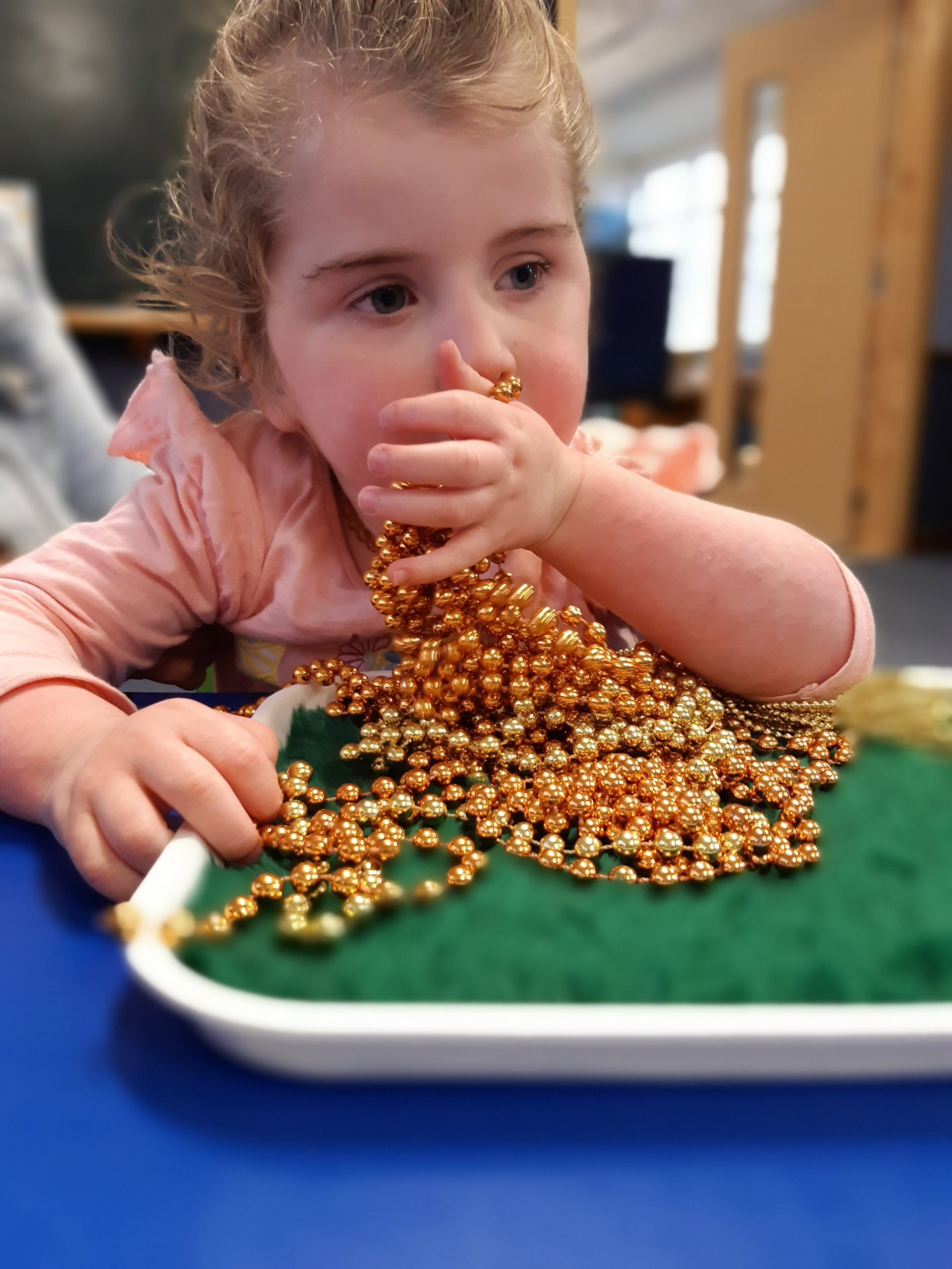 Figure 2 - Child is sitting at a table exploring a string of beads on a tray with her hands 