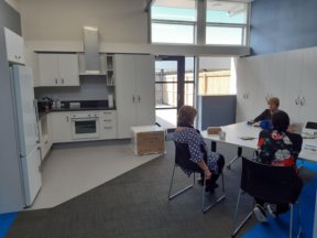 Figure 2 - The new kitchen and kai area at BLENNZ Sensory Resource Centre with 3 people sitting on chairs at a table