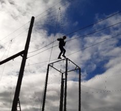 A boy stands on a wire rope while suspended from a safety harness very high up