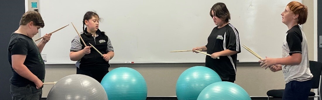 Figure 1 - Four learners are each standing in front of a swiss ball holding drum sticks ready to make drumming noise