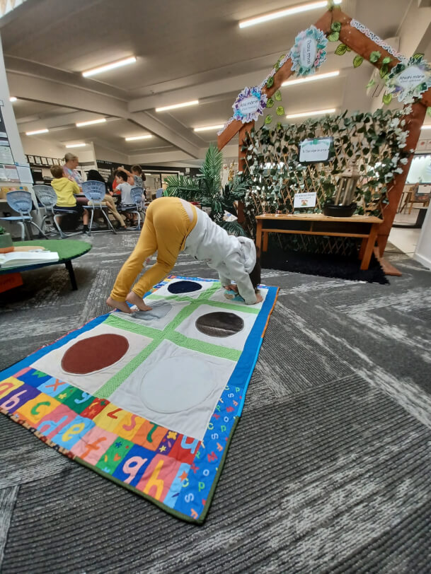 Figure 3 - Child is on all fours on the Twister game mat on the floor. She is making an ‘i’ with her body. Her legs are on Dot 2, and her arms in Dot 4. Each dot is made from a different texture fabric.   