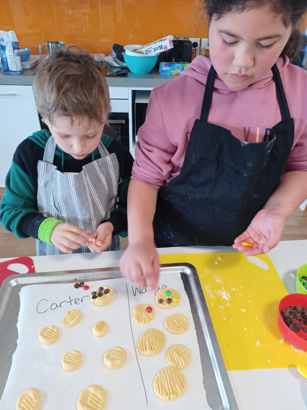 Figure 2 - A boy and girl wearing aprons place decorations onto cookies on a tray