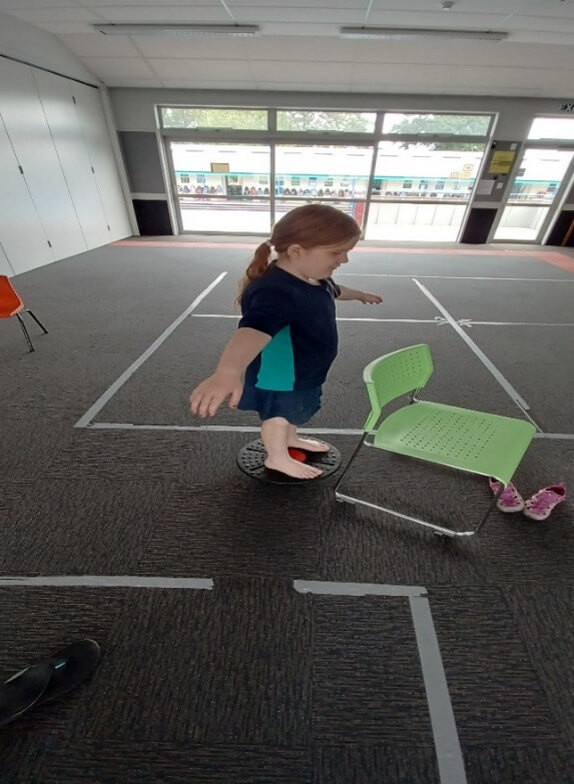 Figure 2 - Laura is in a classroom standing on a balance board practising balancing activities with her RTV prior to the Athletics Day