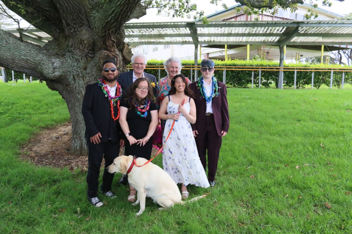 Figure 1 - 6 people and a dog are standing as a group getting their photo taken outside
