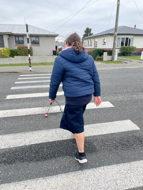 Figure 1 - Tahlia is crossing the road on a zebra crossing using her cane.
