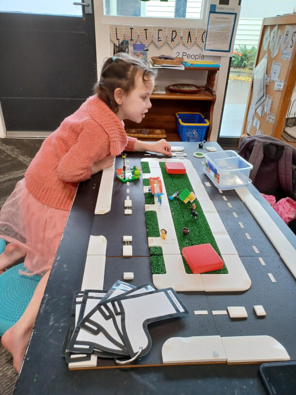 Figure 1 - A child is using the Wise Walker road kit that is set out on a table in the classroom. A set of boot shaped cue cards connected with a book-ring are on the bottom left corner of the kit
