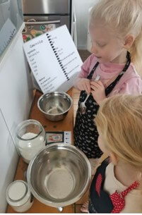Figure 1 - 2 girls standing at a bench with their mixing bowls baking