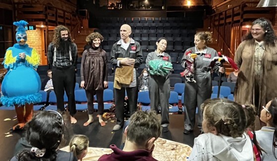 Figure 3 - Seven actors standing on a stage describing their character and costume to a group of learners during the touch tour prior to the the performance