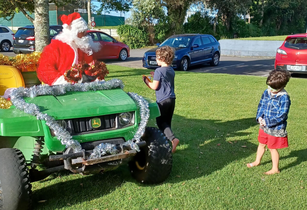 Figure 2 - Father Christmas sitting on a green tractor talking to 2 young boys who are standing on the grass next to his tractor